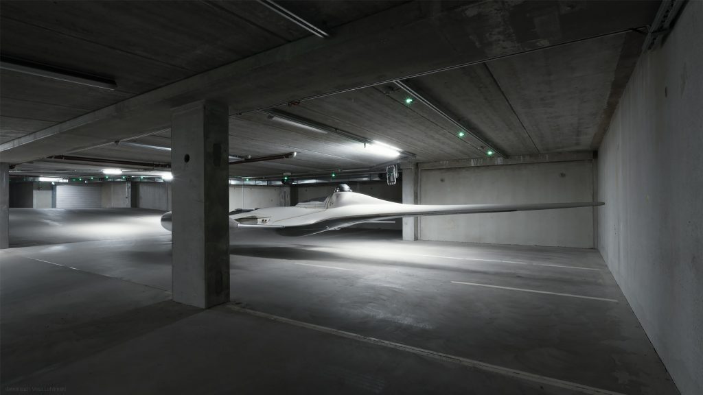 A Naboo N-1 starfighter hovering still inside an empty parking garage with bare concrete walls. 